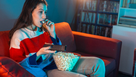 Woman sat on sofa eating popcorn without focusing mindful eating intuitive eating